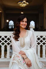Woman in a white traditional outfit sitting on a decorative balcony.