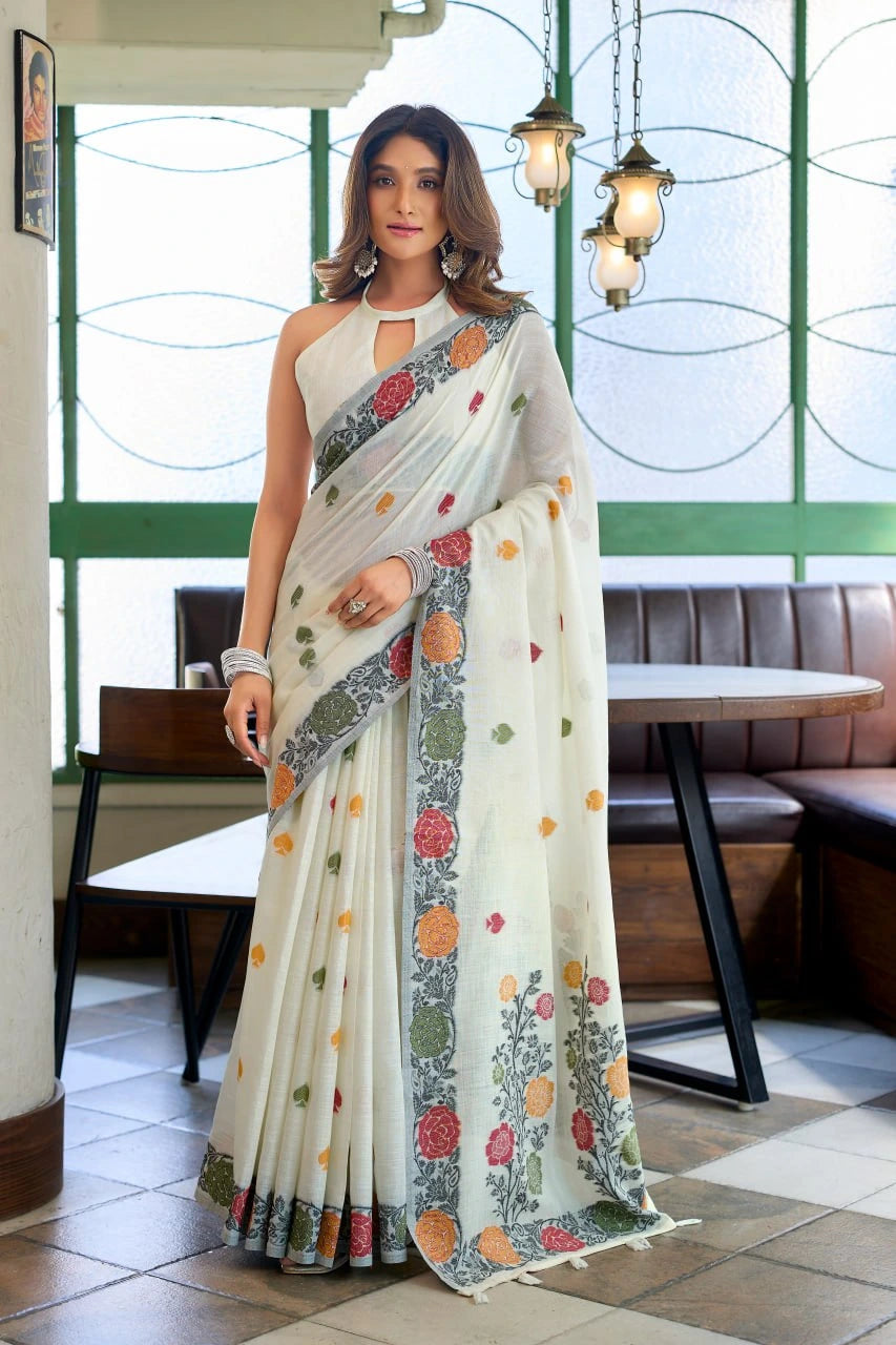 Woman wearing a floral saree in an indoor setting with tables and chairs.