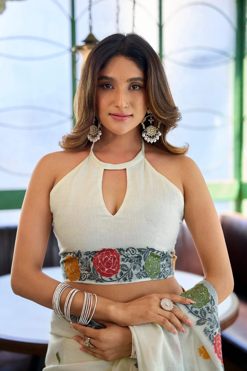 Woman wearing a white top with floral patterns and jewelry indoors.