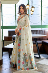 Woman wearing a floral saree in an indoor setting with tables and chairs.
