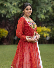 Woman in a red traditional outfit with intricate patterns standing outdoors.