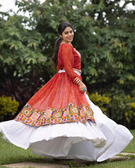 Woman in a traditional red and white outfit with colorful patterns, standing outdoors.