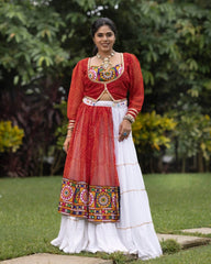 Woman in traditional red and white outfit with colorful embroidery standing outdoors.