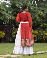 Woman wearing a red and white traditional outfit with a colorful skirt in an outdoor setting.