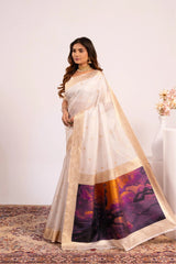 Woman wearing a white saree with a colorful design, standing against a plain background.