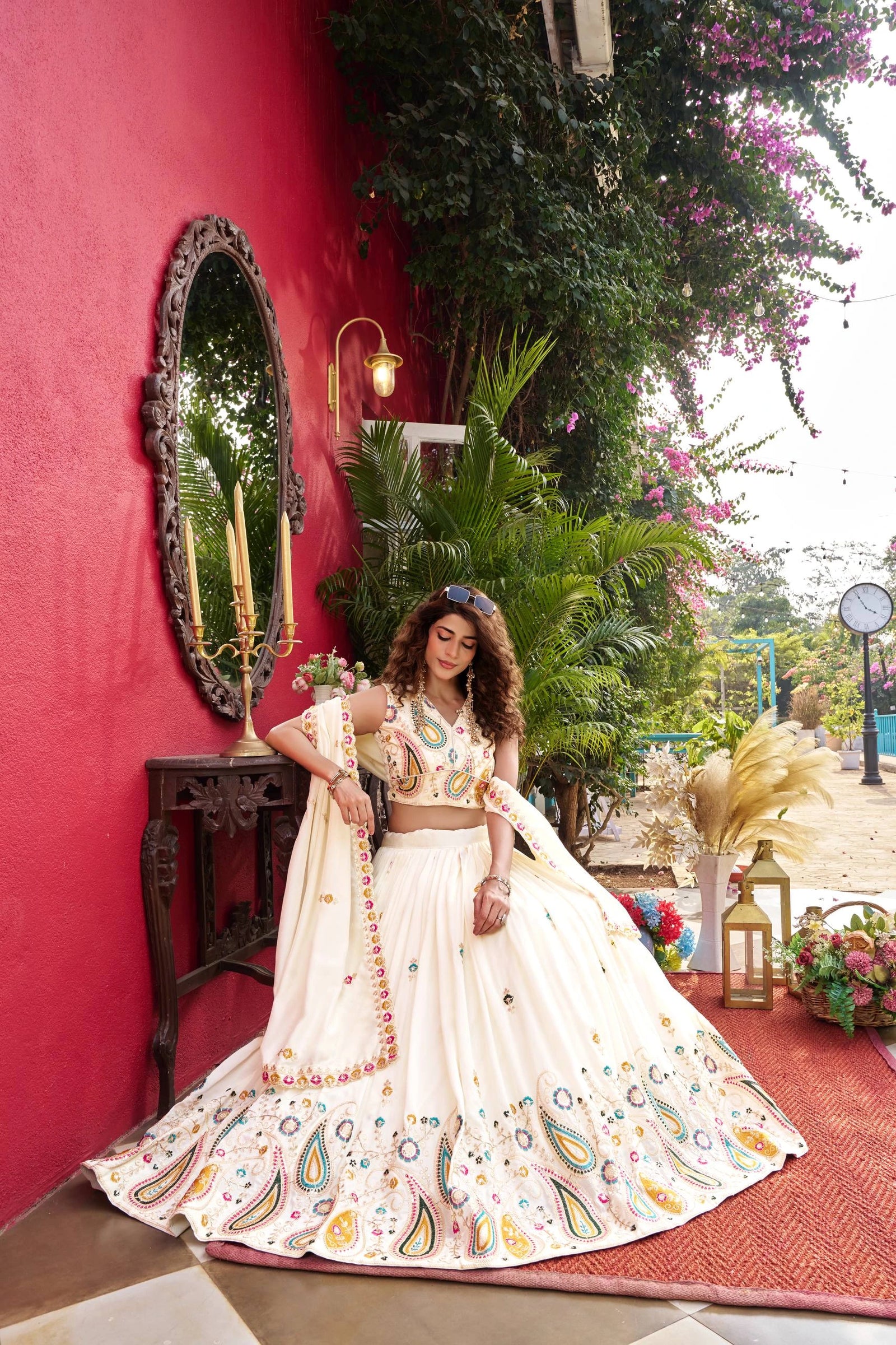 Woman in a traditional outfit standing in front of a red wall with decorative elements.