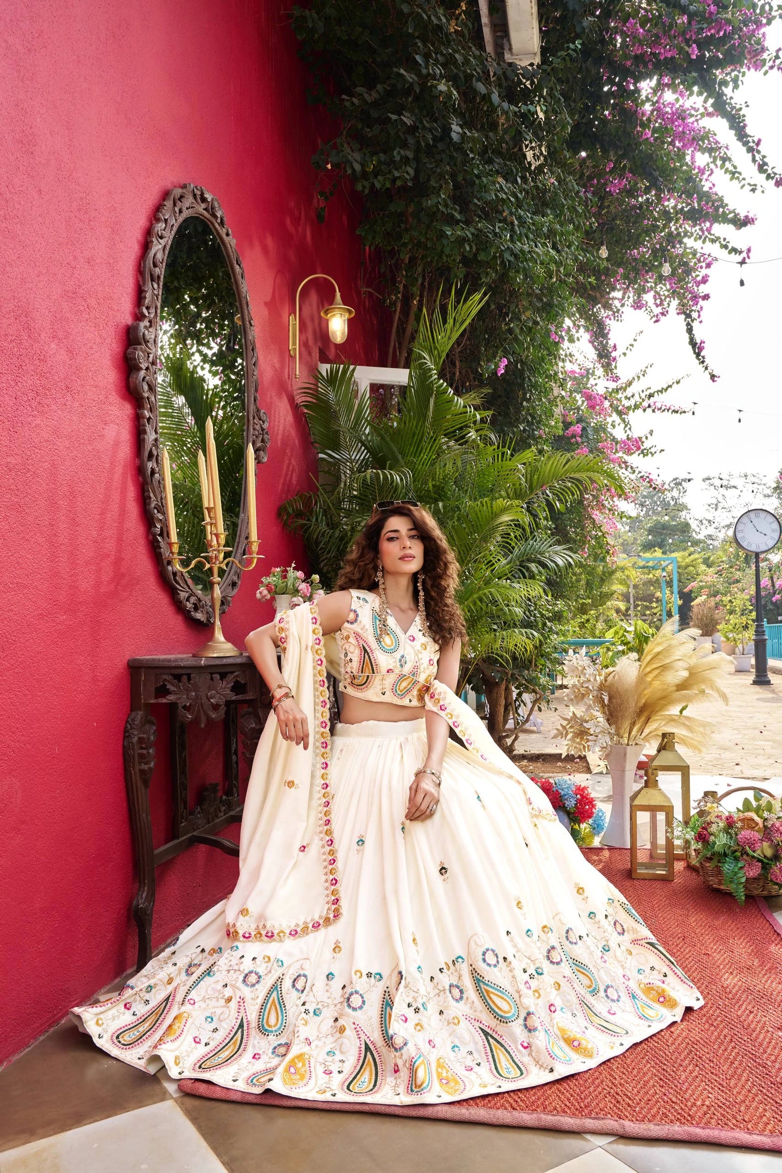 Woman in a traditional outfit standing in front of a red wall with decorative elements.