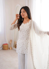 Woman wearing a white embroidered outfit with a sheer dupatta in a softly lit room.