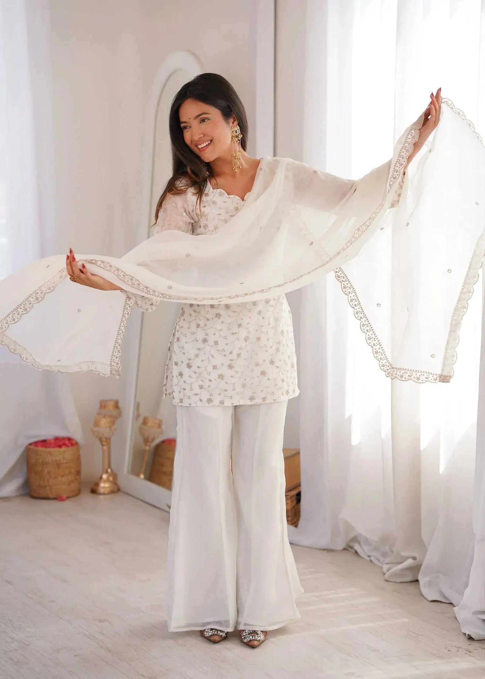 Woman in a white traditional outfit with a sheer dupatta in a bright room.