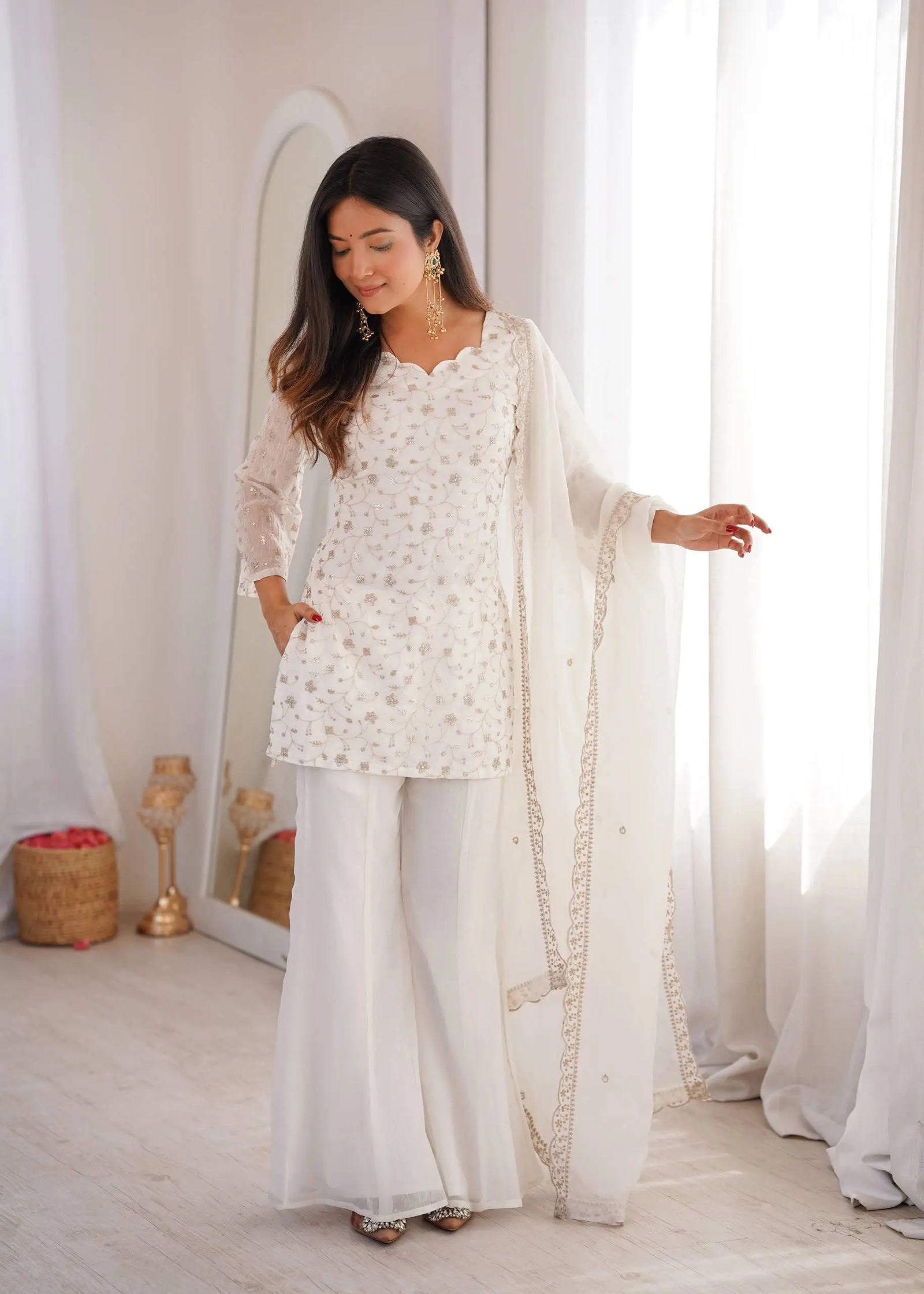 Woman wearing a white traditional outfit with a dupatta in a bright room.