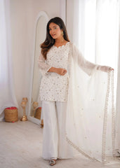 Woman in a white traditional outfit with a sheer dupatta, standing in a bright room.