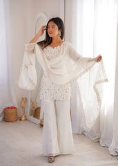 Woman in a white traditional outfit with a dupatta, standing in a bright room.