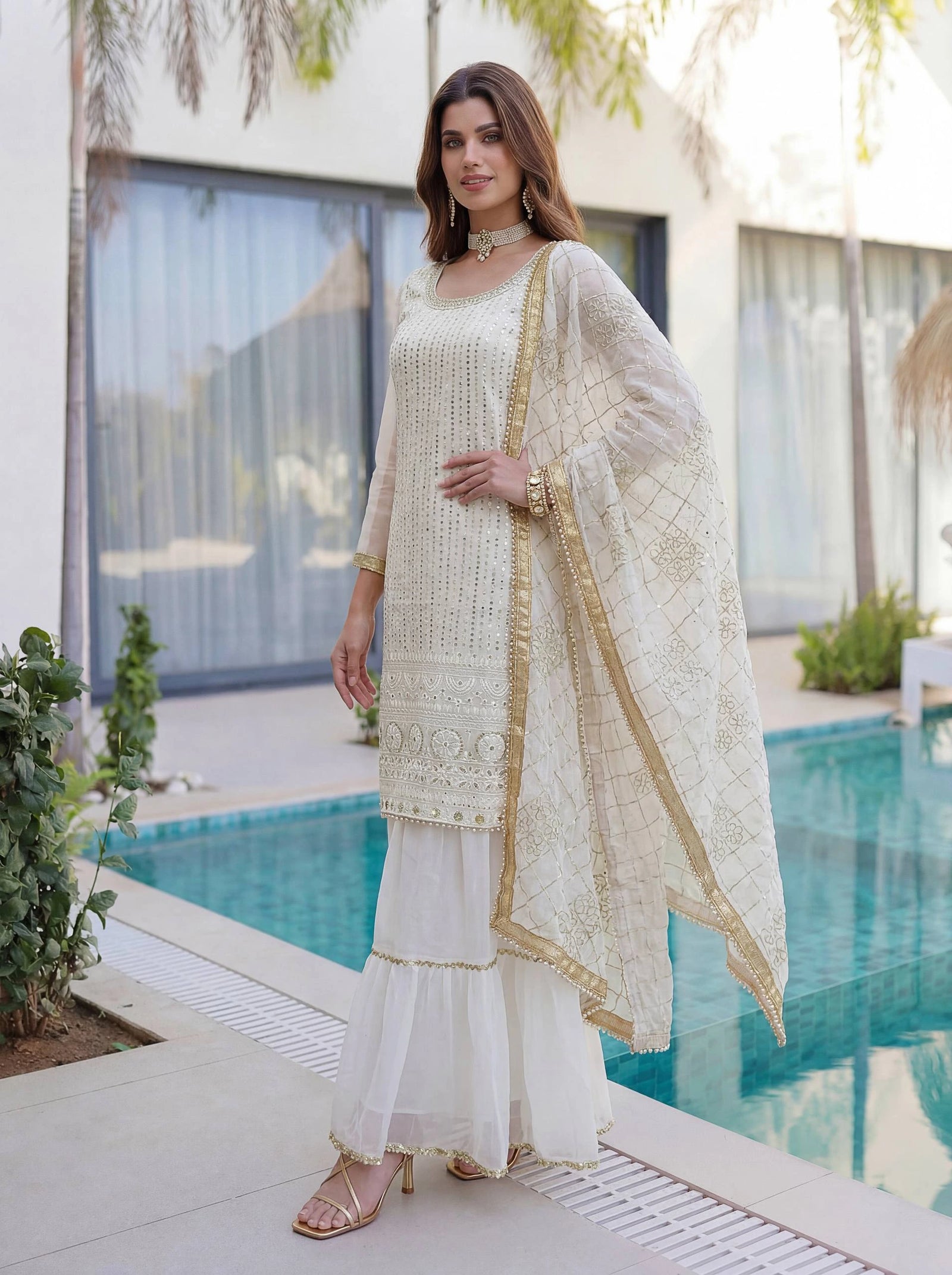 Woman in a white and gold traditional outfit standing by a pool.