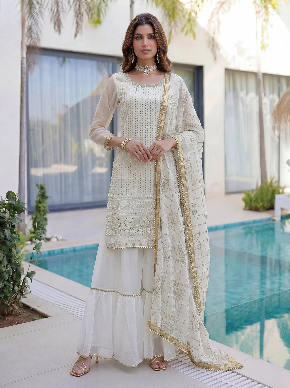 Woman in a white and gold traditional outfit standing by a pool.