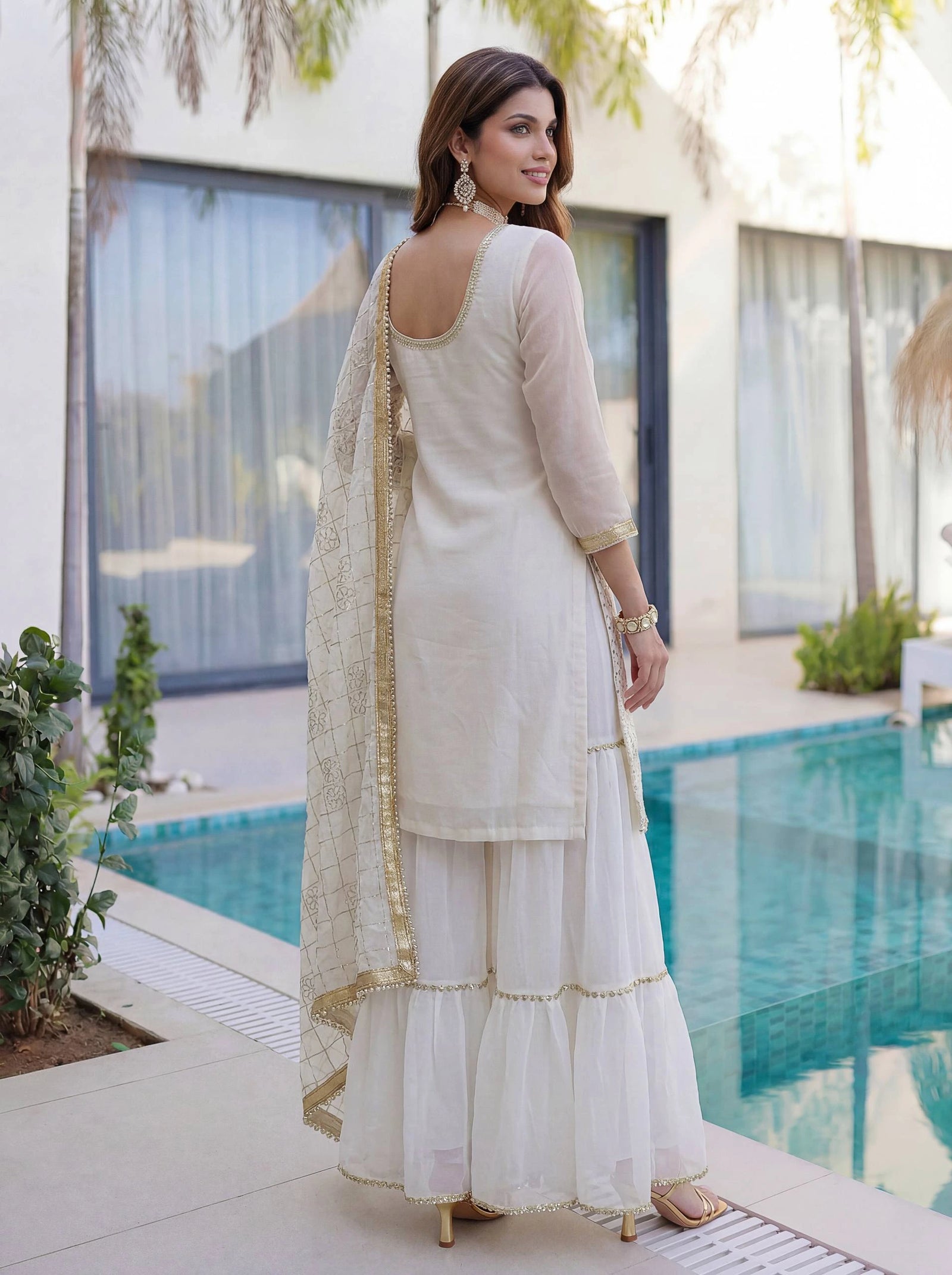 Woman in a white traditional outfit standing by a poolside.