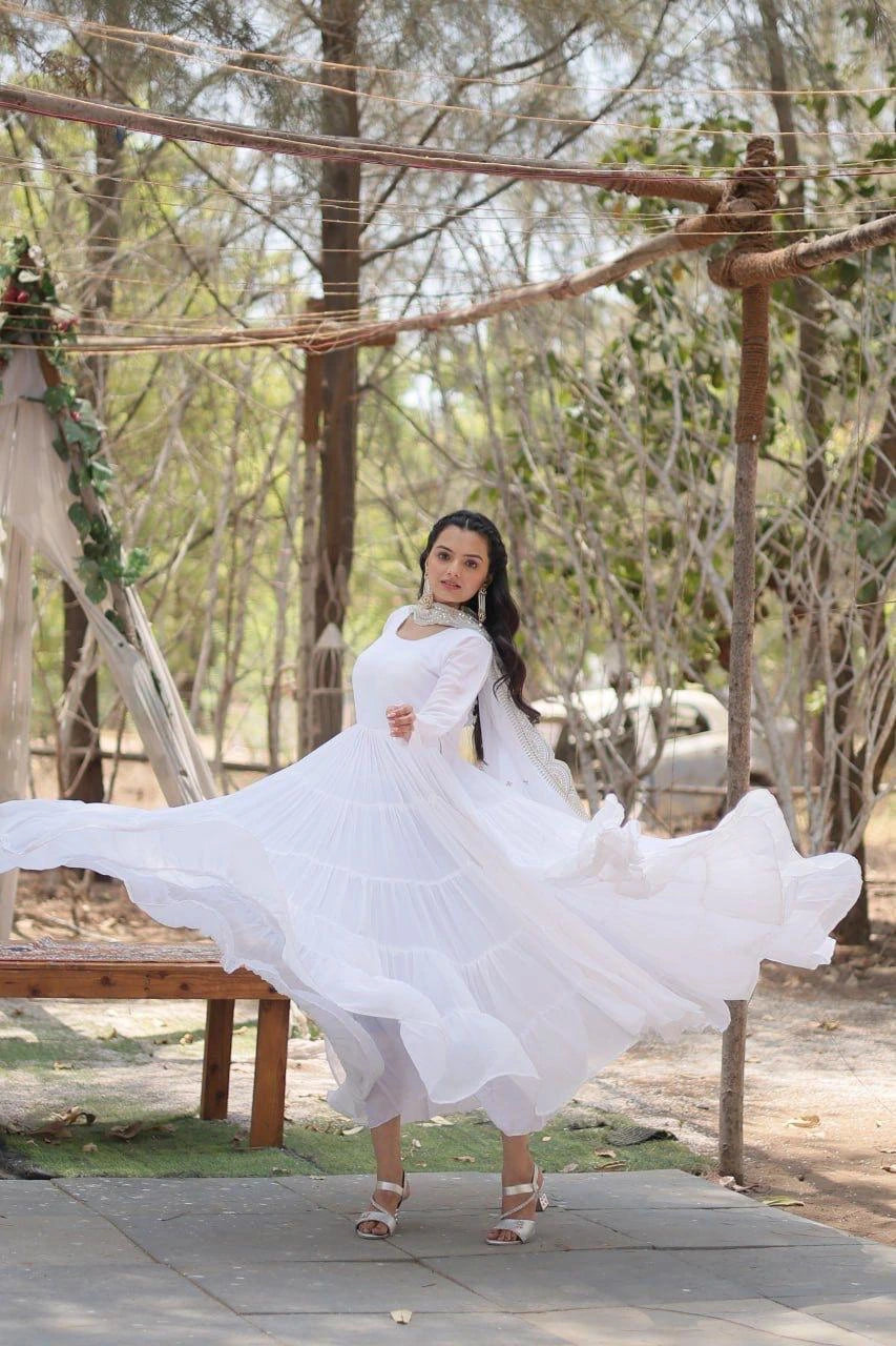 Woman in a white dress standing outdoors with trees and a wooden structure in the background