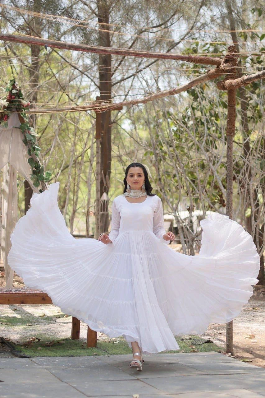 Woman in a white dress standing outdoors with trees and wooden structures in the background