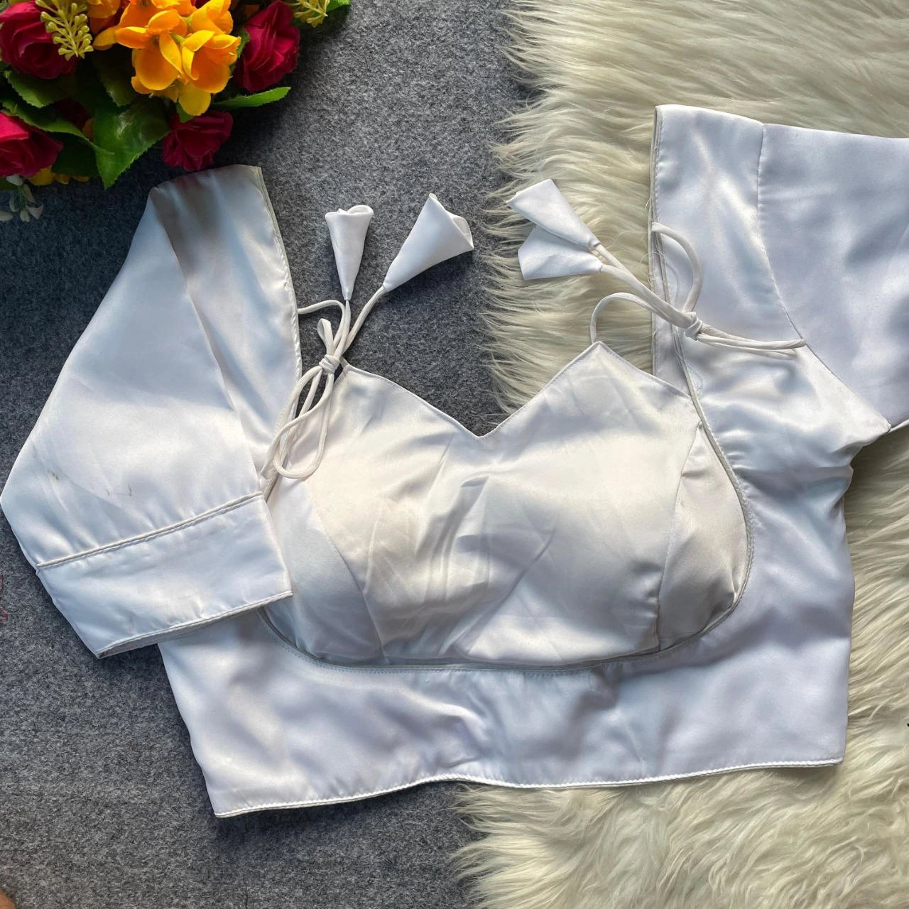 White satin top with bow details on a textured surface with flowers in the corner.