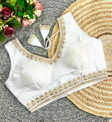 White blouse with gold embroidery on a textured surface with flowers and a fan.