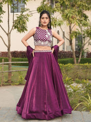 Woman in a purple traditional outfit standing outdoors with greenery in the background