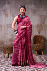 Woman in a pink saree standing in a room with patterned walls and furniture.
