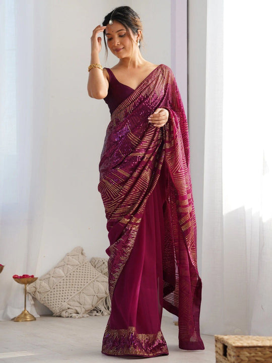 Woman wearing a maroon saree with gold patterns in a minimal indoor setting