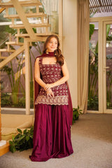 Woman in a maroon traditional outfit standing indoors with decorative elements.