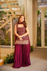 Woman in a maroon traditional outfit standing indoors with decorative elements.