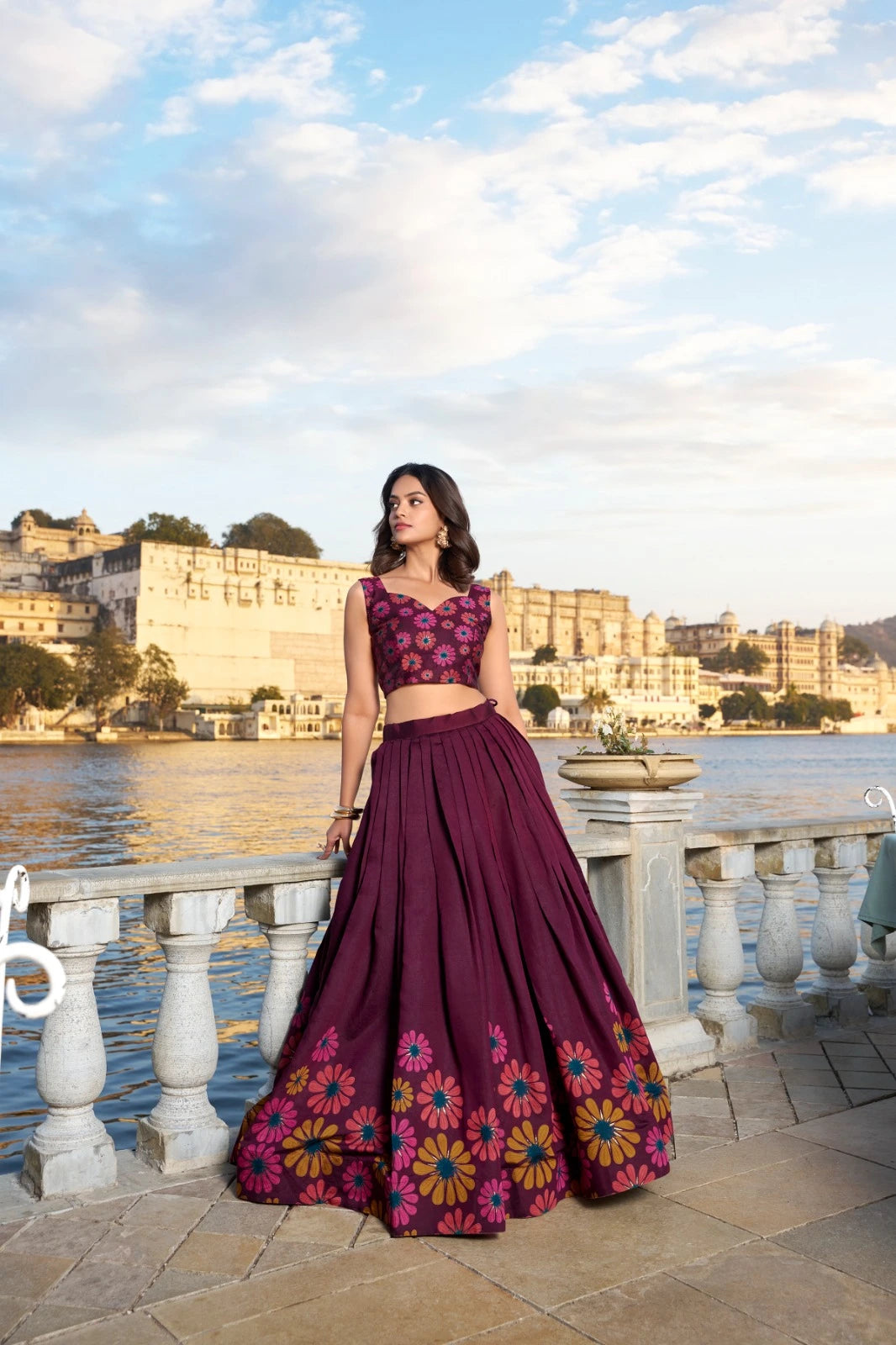 Woman in a traditional outfit standing by a waterfront with a scenic background