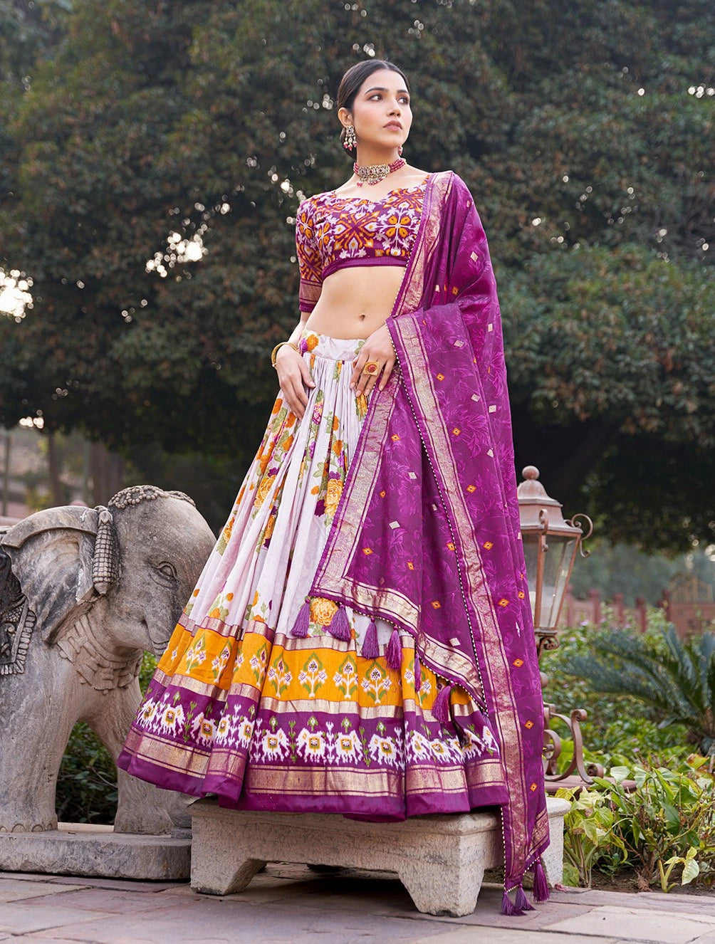 Woman in traditional Indian attire with a purple blouse and white and orange skirt, standing outdoors.