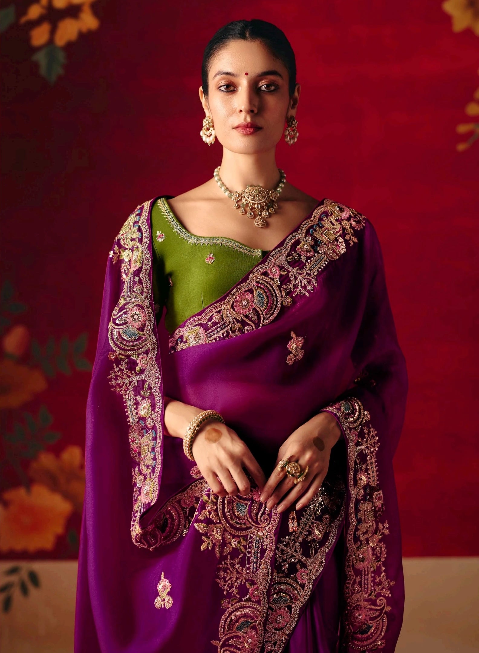 Woman wearing a purple saree with green blouse against a red background