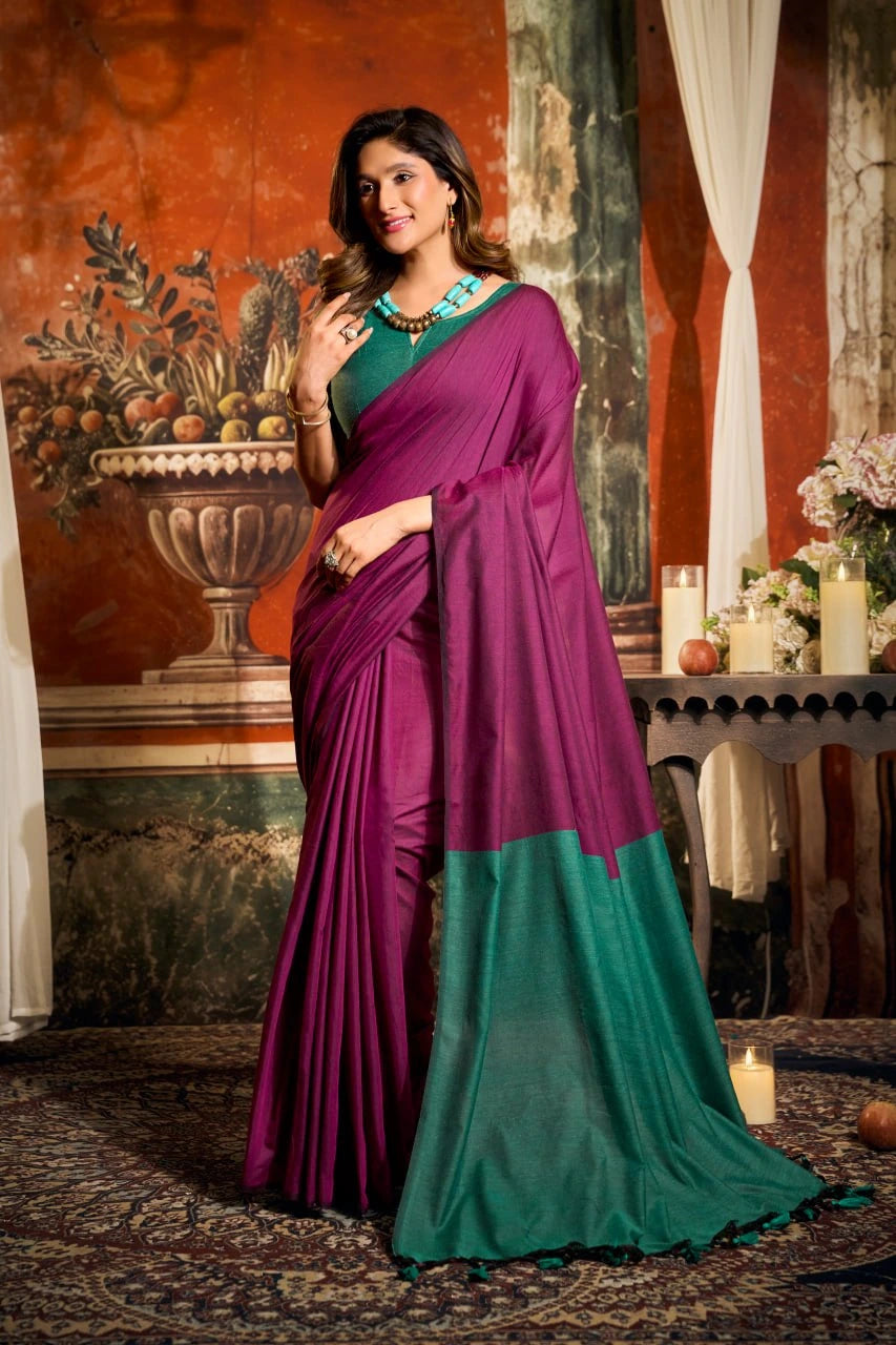 Woman in a purple and green saree standing in an elegant room with decorative elements.