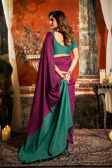 Woman in a green and purple saree standing in a room with decorative wall art.