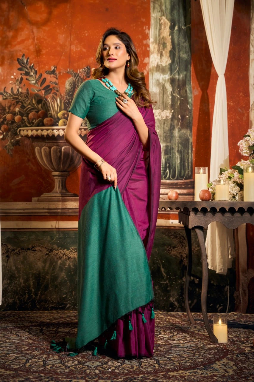 Woman in a purple and green saree standing in an ornate room.