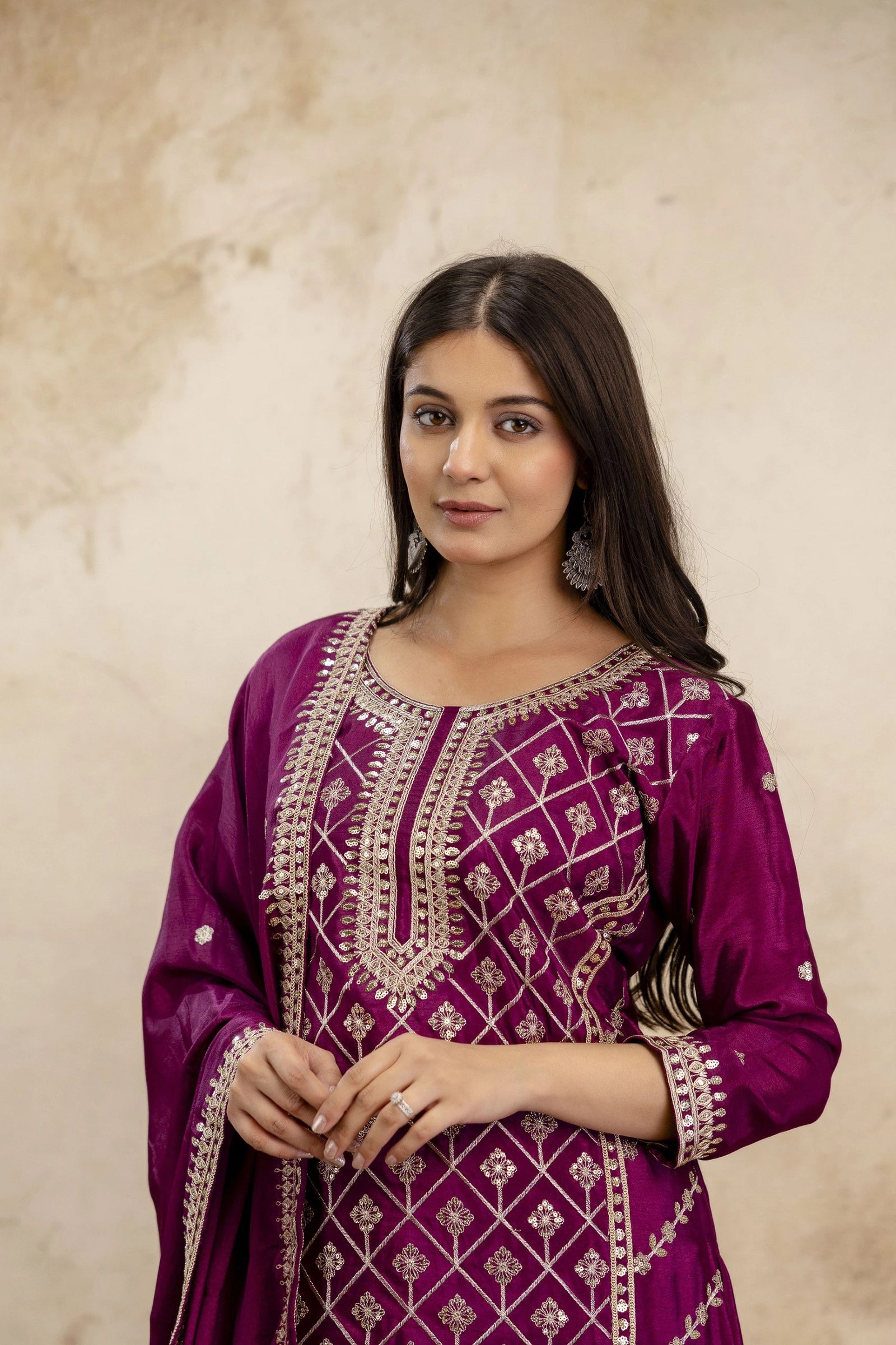 Woman wearing a purple embroidered traditional outfit against a beige background
