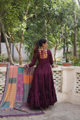 Woman in a purple dress standing on a balcony with a colorful quilt and greenery.