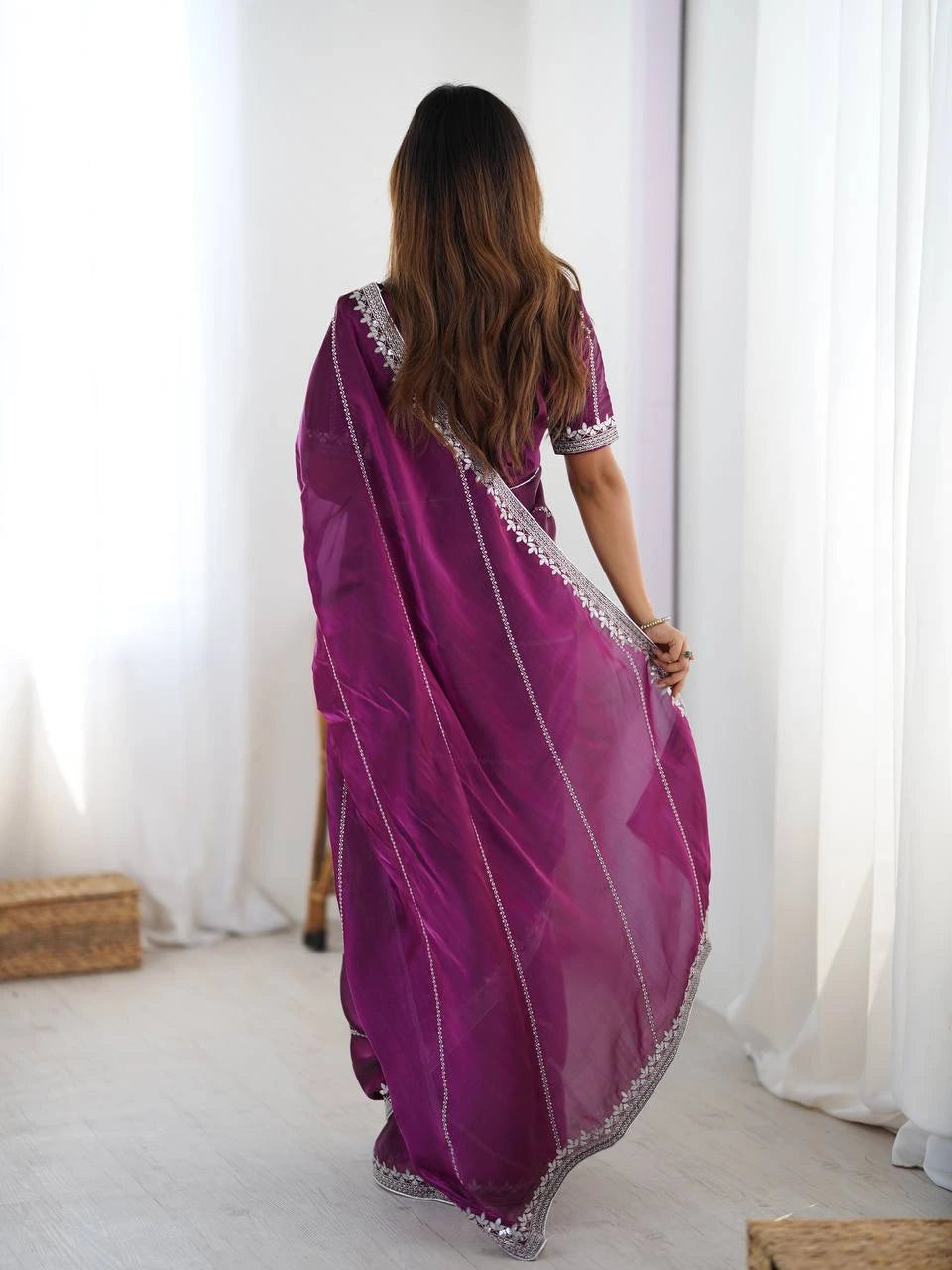Woman wearing a purple saree with white border in a minimalistic room.