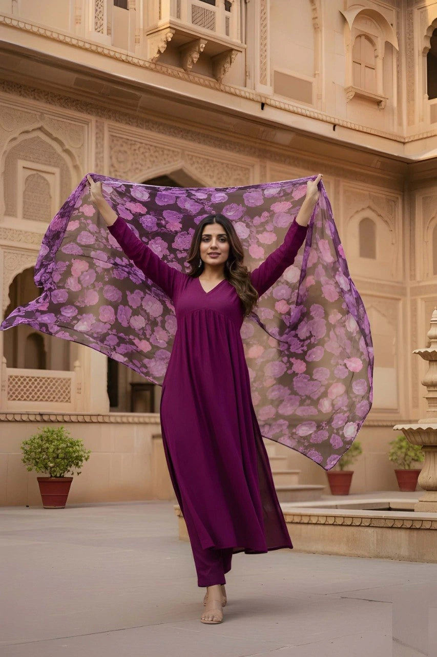 Woman in a purple dress holding a floral scarf in front of an architectural building.