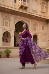 Woman in a purple traditional outfit with a floral scarf standing in front of an architectural building.