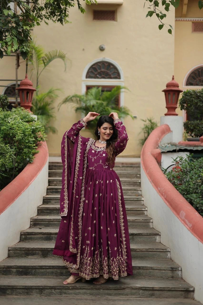 Woman in a purple traditional outfit standing on a staircase with a building and greenery in the background