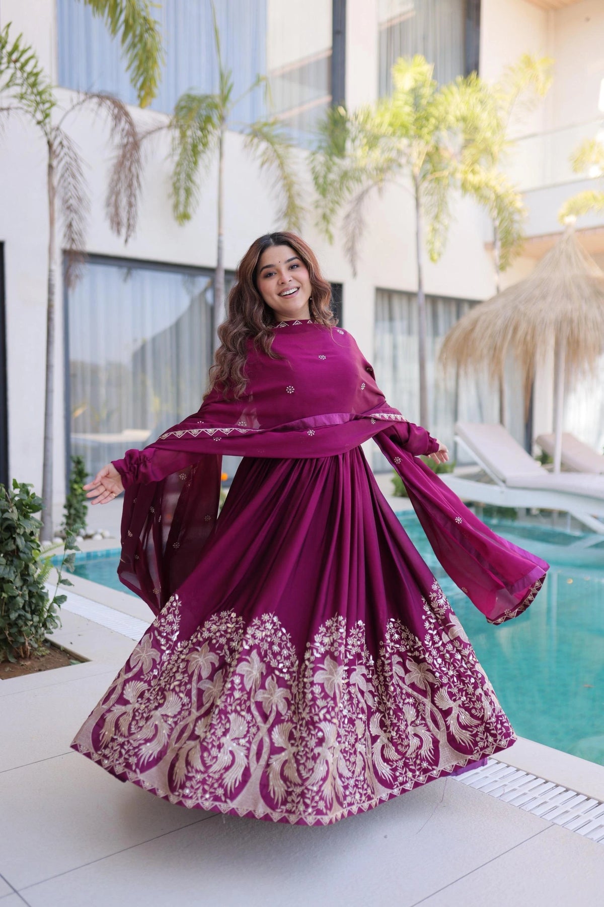 Woman in a purple dress with white embroidery standing by a pool.