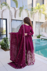 Woman in a burgundy traditional outfit by a poolside with modern building and greenery in the background