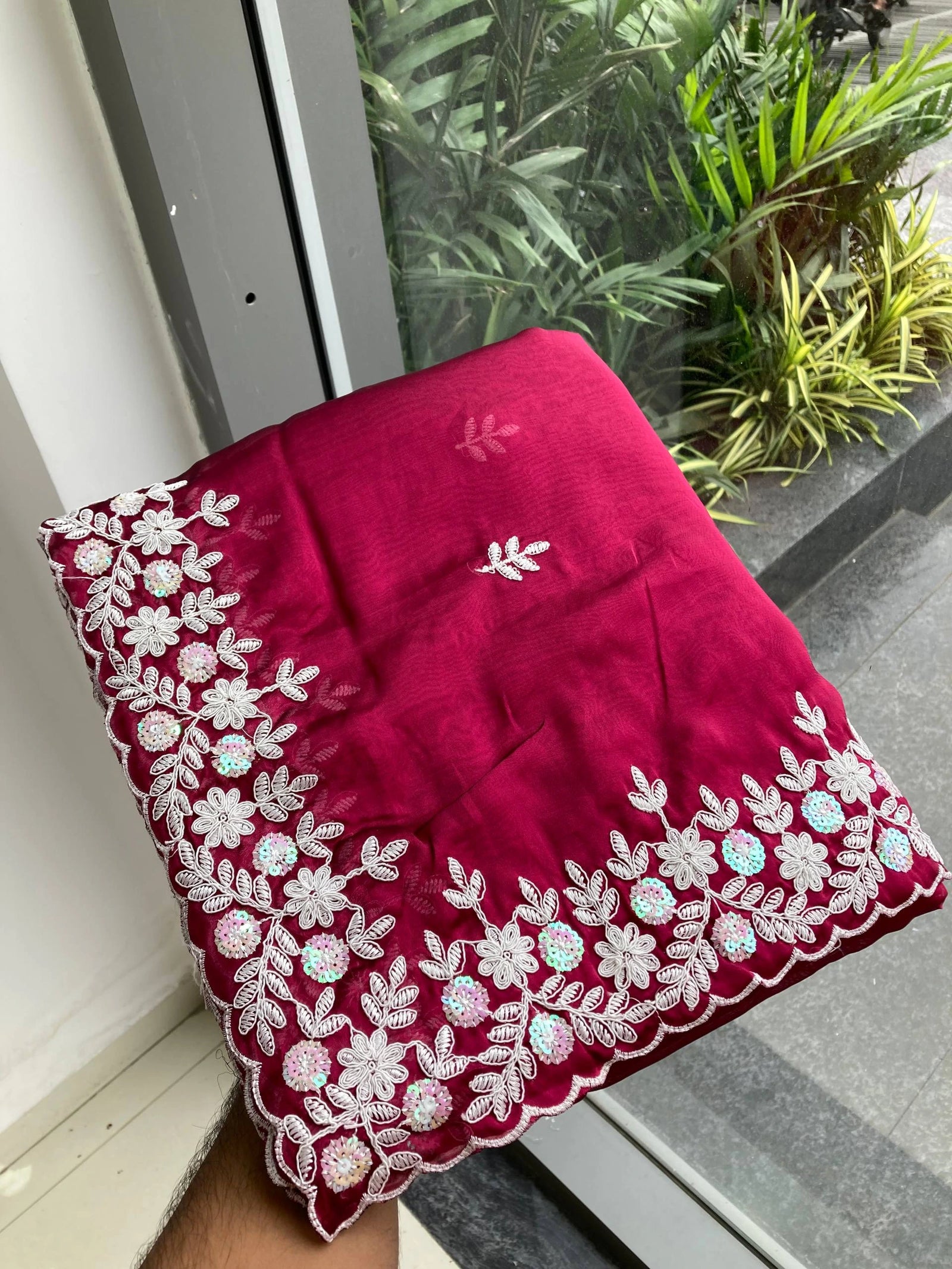 Red embroidered fabric held by a hand with plants in the background