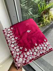 Red embroidered fabric held by a hand with plants in the background