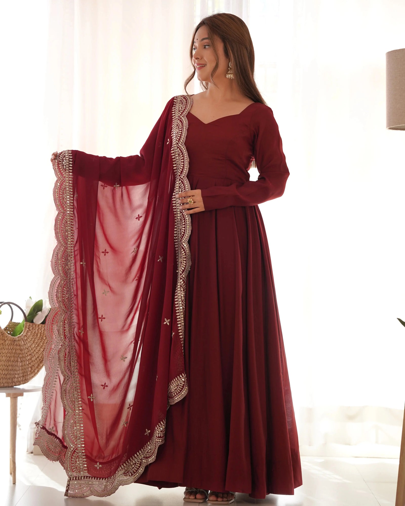 Woman wearing a maroon traditional outfit with a matching dupatta in a bright room.