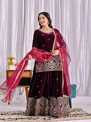 Woman in a dark purple traditional outfit with pink dupatta against a white curtain background
