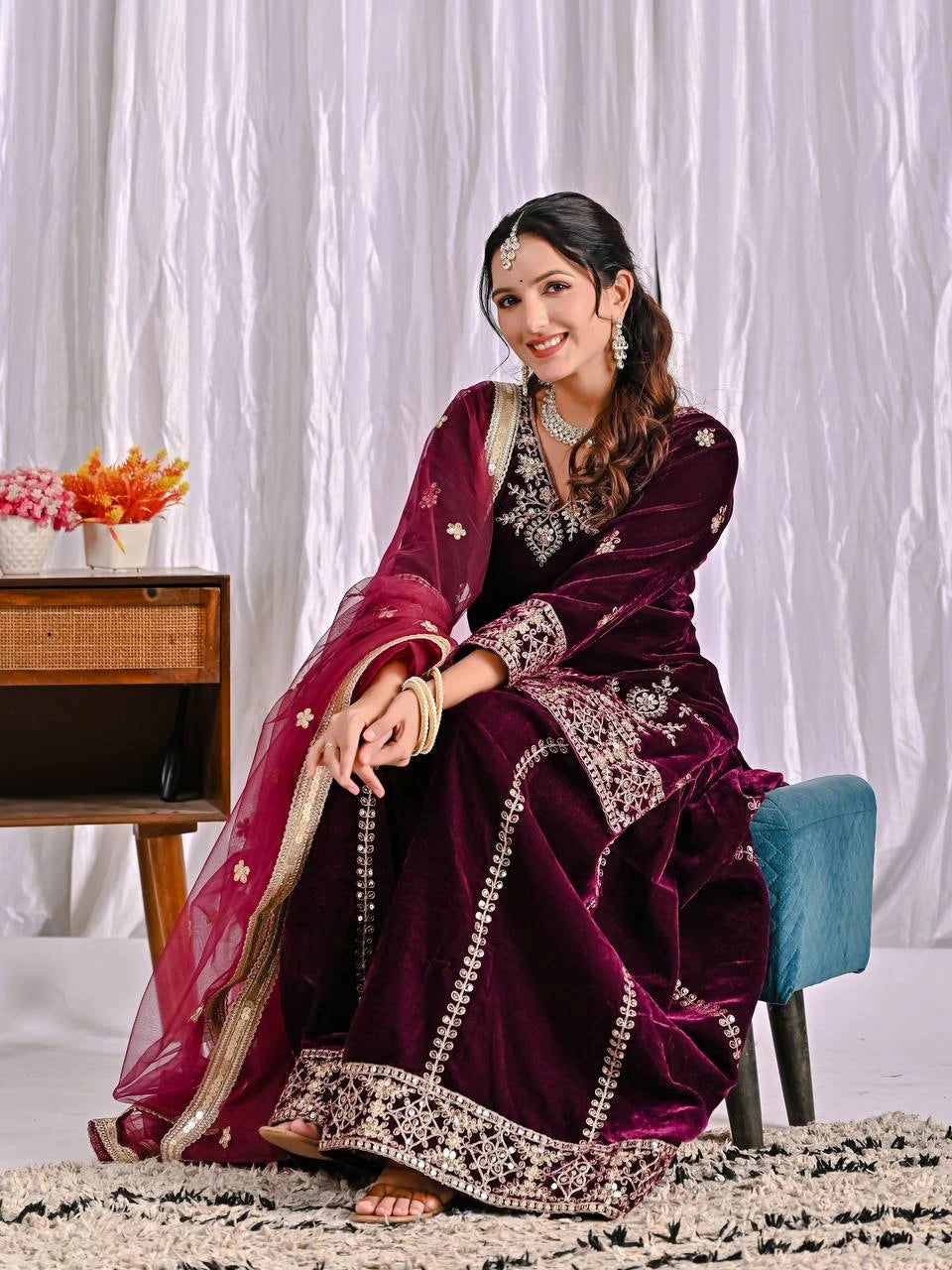 Woman in a traditional maroon outfit with white embroidery sitting on a chair.