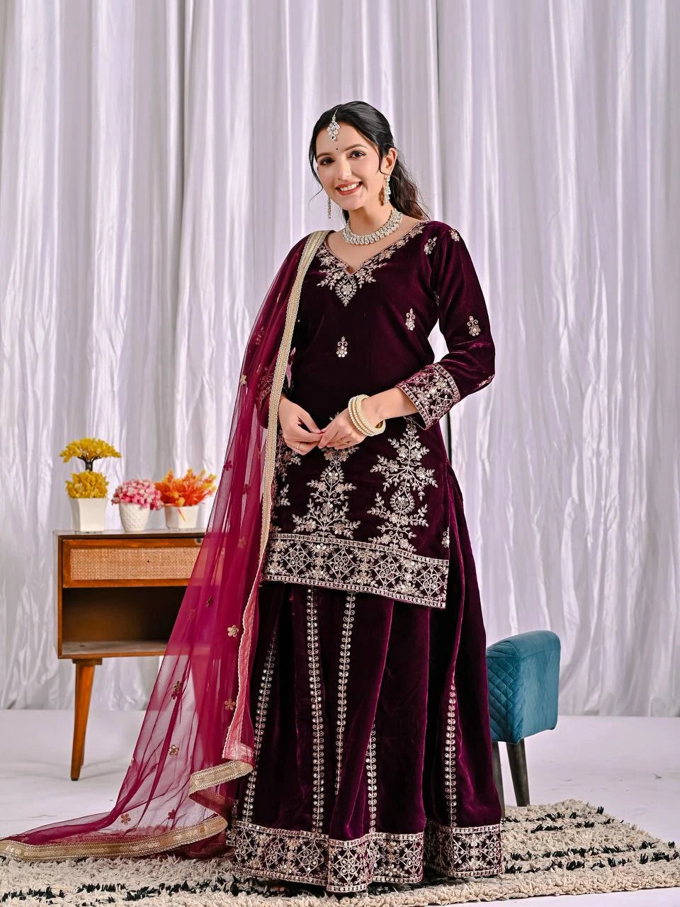 Woman in a maroon traditional outfit with white embroidery against a white curtain background