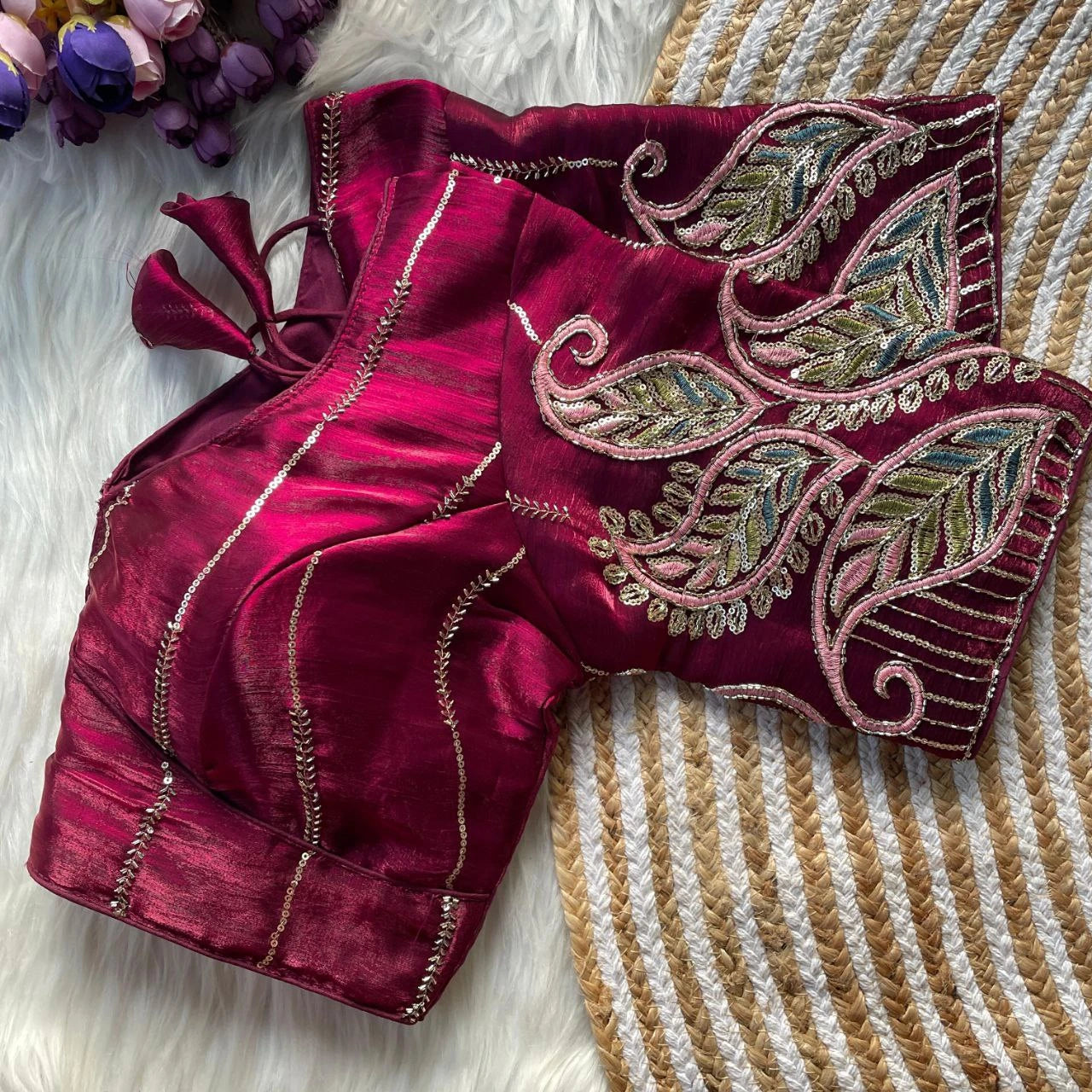 Maroon embroidered blouse on a textured surface with flowers in the background
