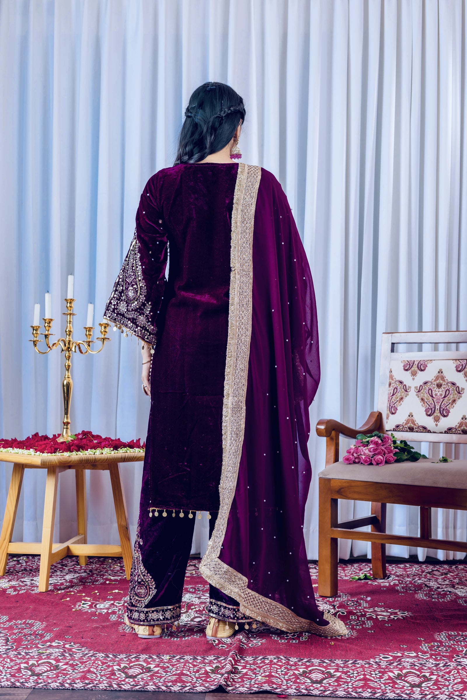 Person wearing a dark purple traditional outfit with gold details in a decorated room.